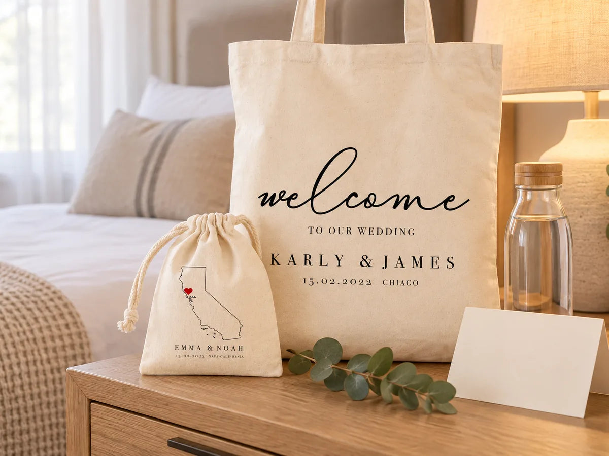 Chambre d'hôtel à la lumière chaude d'une lampe : sac d'accueil Karly & James debout sur une commode en chêne, pochon à carte de Californie devant, bouteille d'eau en verre, carte de bienvenue vierge et eucalyptus